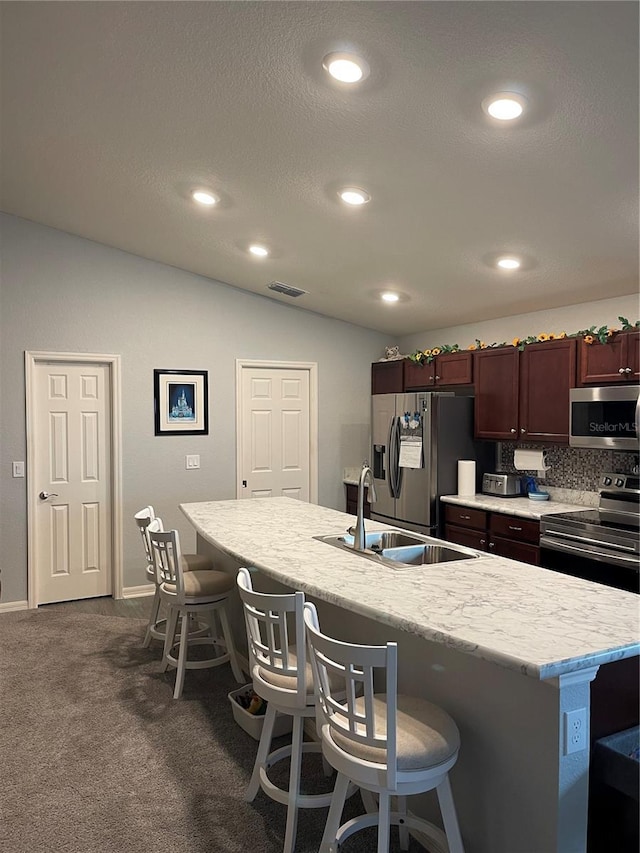 kitchen with stainless steel appliances, tasteful backsplash, a kitchen island with sink, a kitchen breakfast bar, and sink