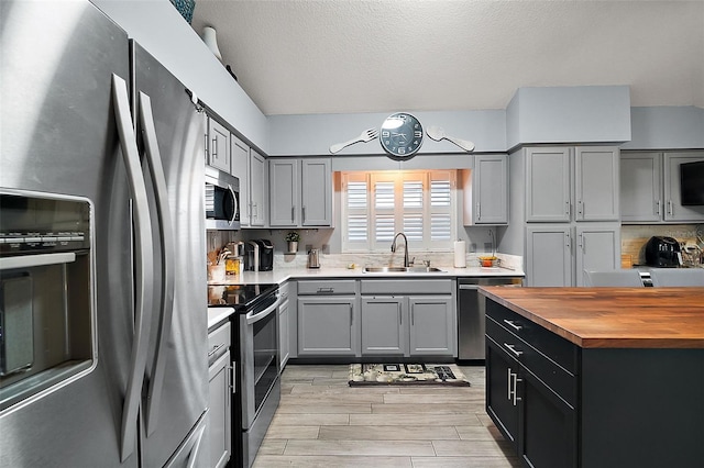 kitchen with sink, a textured ceiling, light hardwood / wood-style flooring, decorative backsplash, and appliances with stainless steel finishes