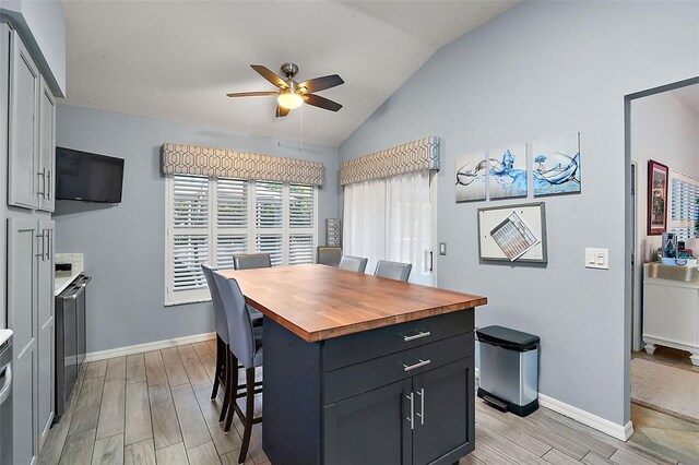 kitchen featuring vaulted ceiling, wood counters, ceiling fan, a kitchen bar, and a kitchen island