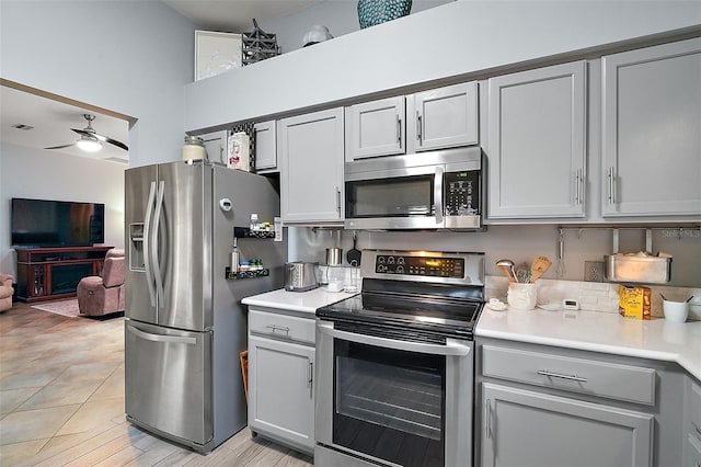 kitchen with a high ceiling, appliances with stainless steel finishes, ceiling fan, and gray cabinets