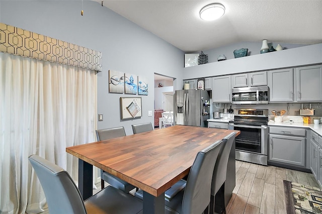 kitchen featuring gray cabinetry, stainless steel appliances, lofted ceiling, and a textured ceiling