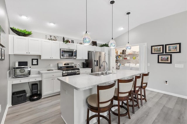 kitchen featuring stainless steel appliances, washer and dryer, hanging light fixtures, vaulted ceiling, and sink