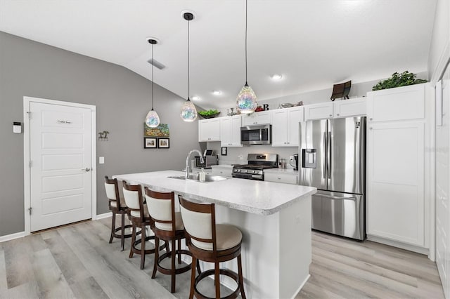 kitchen featuring appliances with stainless steel finishes, decorative light fixtures, white cabinetry, sink, and a kitchen island with sink