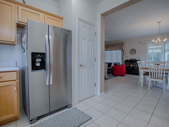 kitchen featuring light tile patterned floors, light brown cabinetry, stainless steel fridge, pendant lighting, and a notable chandelier