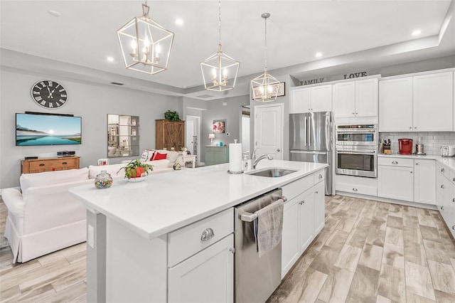 kitchen with appliances with stainless steel finishes, decorative light fixtures, a kitchen island with sink, white cabinets, and sink