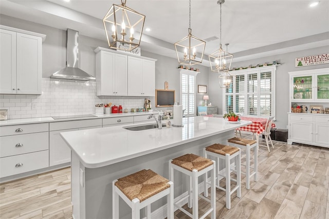 kitchen with sink, wall chimney exhaust hood, pendant lighting, and an island with sink