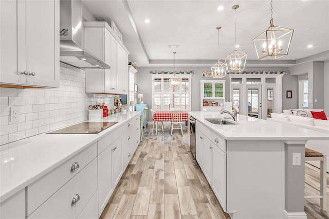 kitchen with sink, a large island with sink, hanging light fixtures, and wall chimney range hood