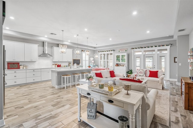 kitchen featuring wall chimney exhaust hood, decorative light fixtures, a kitchen bar, white cabinetry, and a kitchen island with sink