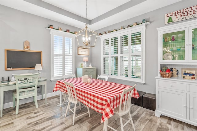 dining room with a notable chandelier, a tray ceiling, and light hardwood / wood-style flooring