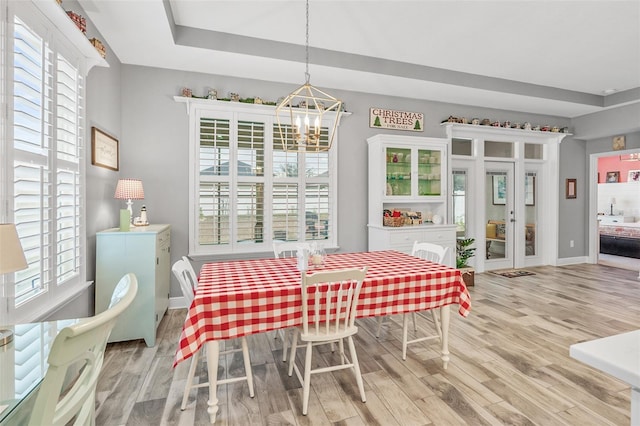 dining room featuring french doors, an inviting chandelier, light hardwood / wood-style flooring, and a tray ceiling