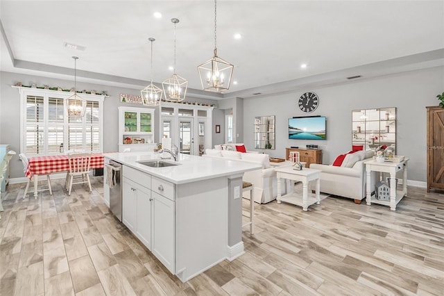 kitchen with dishwasher, pendant lighting, white cabinetry, and a center island with sink