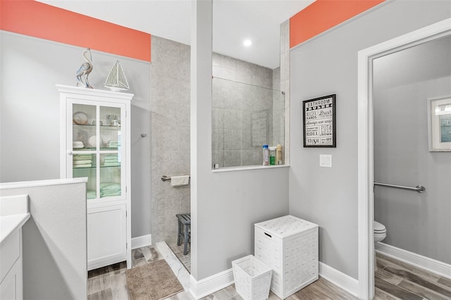 bathroom featuring toilet, vanity, wood-type flooring, and tiled shower