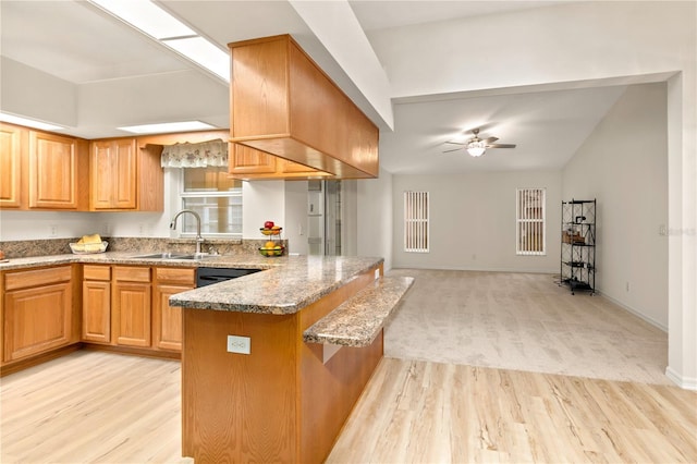 kitchen featuring ceiling fan, a peninsula, a sink, light wood-style floors, and black dishwasher