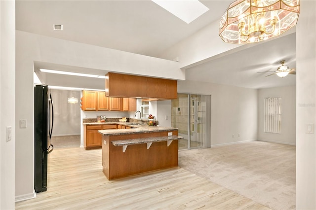 kitchen with freestanding refrigerator, open floor plan, a sink, a peninsula, and a kitchen breakfast bar