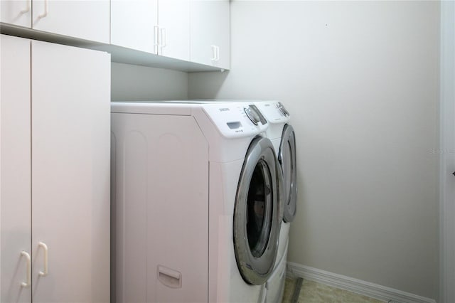 clothes washing area with washing machine and clothes dryer, cabinet space, and baseboards