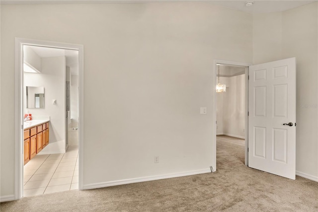 unfurnished bedroom featuring light carpet, light tile patterned floors, baseboards, and connected bathroom