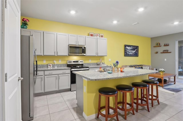 kitchen featuring light stone counters, light tile patterned floors, appliances with stainless steel finishes, a kitchen breakfast bar, and a kitchen island with sink