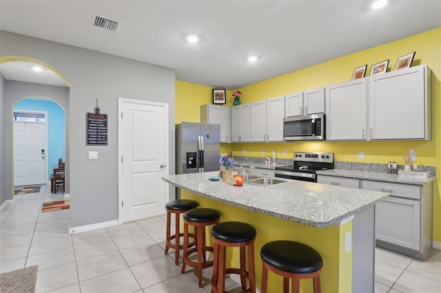 kitchen with light tile patterned floors, a center island with sink, appliances with stainless steel finishes, a kitchen breakfast bar, and light stone counters