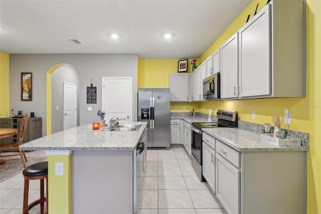 kitchen featuring light tile patterned floors, a kitchen island with sink, appliances with stainless steel finishes, and a kitchen breakfast bar