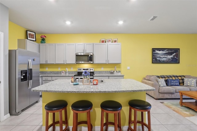 kitchen with a kitchen island with sink, light stone counters, a breakfast bar area, and stainless steel appliances