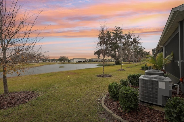 yard at dusk featuring central air condition unit and a water view