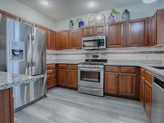 kitchen featuring light hardwood / wood-style floors, light stone counters, stainless steel appliances, and a textured ceiling