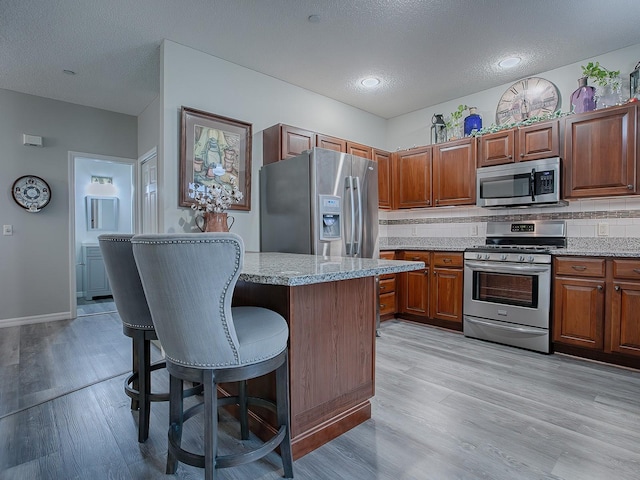 kitchen with a textured ceiling, a breakfast bar area, stainless steel appliances, and tasteful backsplash