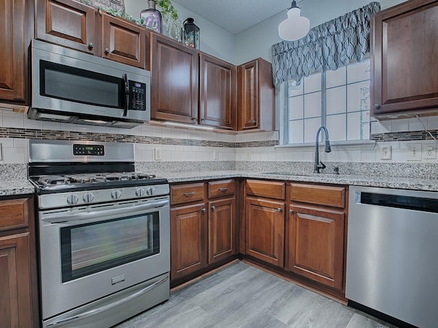 kitchen with appliances with stainless steel finishes, decorative backsplash, light wood-type flooring, light stone counters, and sink