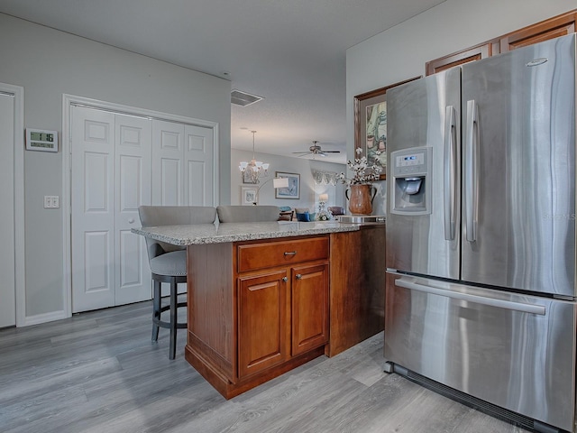 kitchen with stainless steel refrigerator with ice dispenser, a breakfast bar area, hanging light fixtures, ceiling fan with notable chandelier, and a center island