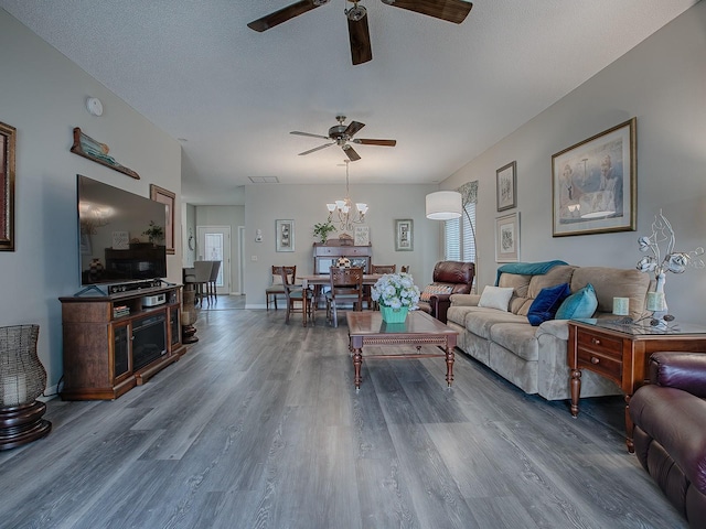 living room featuring ceiling fan with notable chandelier, hardwood / wood-style floors, and a textured ceiling