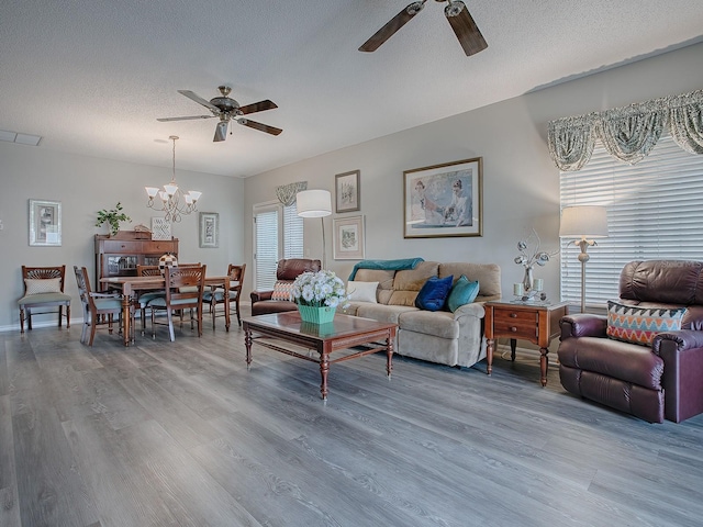 living room with wood-type flooring, ceiling fan with notable chandelier, and a textured ceiling