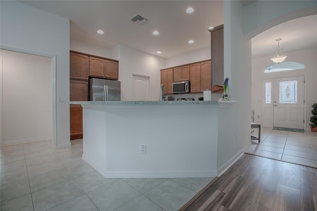 kitchen featuring light wood-type flooring, kitchen peninsula, appliances with stainless steel finishes, and decorative light fixtures