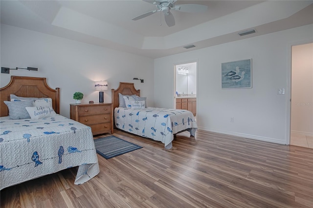 bedroom with ceiling fan, hardwood / wood-style floors, ensuite bathroom, and a raised ceiling