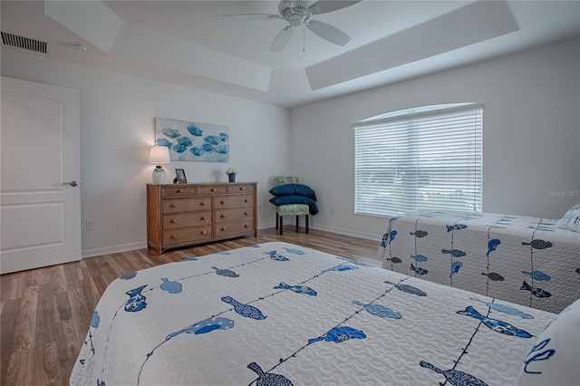 bedroom featuring hardwood / wood-style flooring, ceiling fan, and a raised ceiling