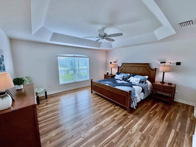 bedroom with a tray ceiling, ceiling fan, and dark hardwood / wood-style flooring