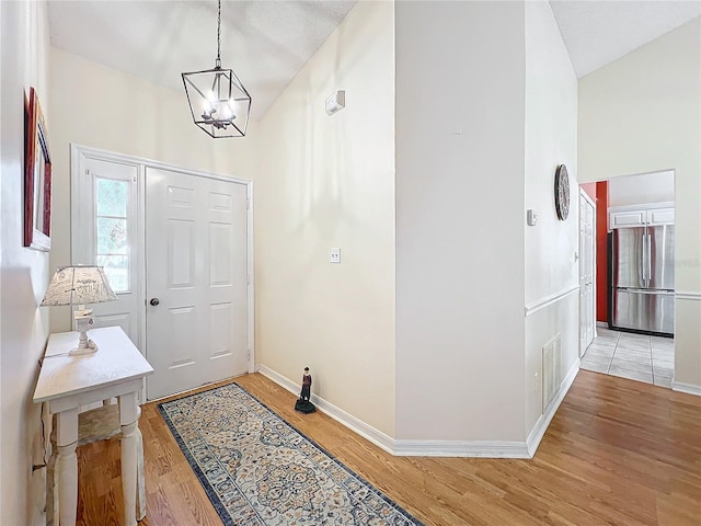 foyer with light wood-type flooring, vaulted ceiling, and a notable chandelier