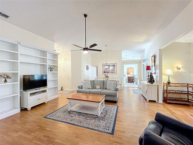 living room featuring a textured ceiling, light wood-type flooring, vaulted ceiling, and ceiling fan with notable chandelier