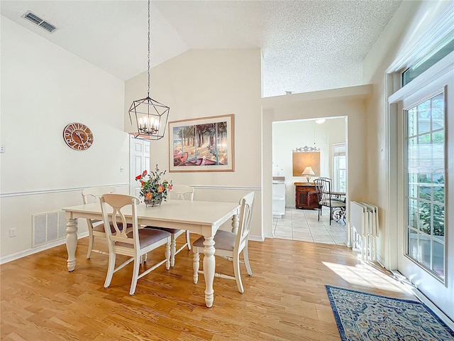 dining room featuring a textured ceiling, light wood-type flooring, vaulted ceiling, and a notable chandelier