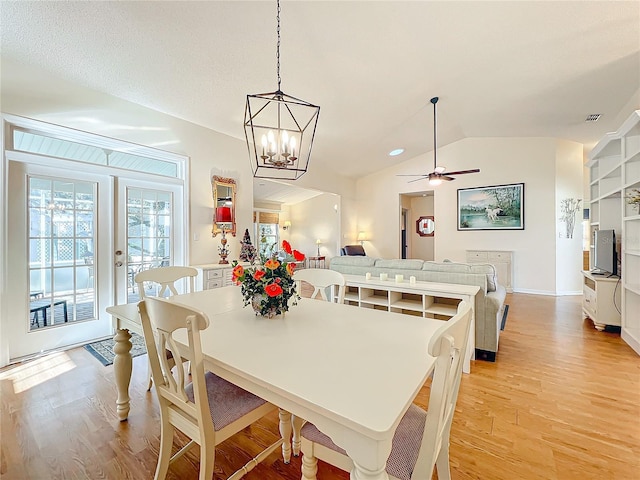 dining space featuring ceiling fan with notable chandelier, built in features, vaulted ceiling, and light hardwood / wood-style flooring