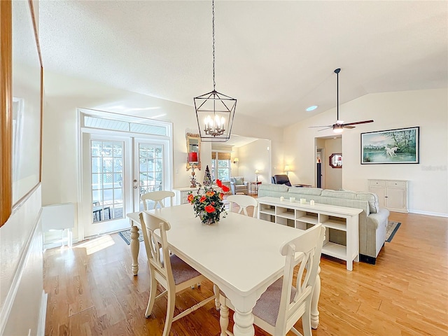 dining space with ceiling fan with notable chandelier, french doors, vaulted ceiling, and light hardwood / wood-style flooring