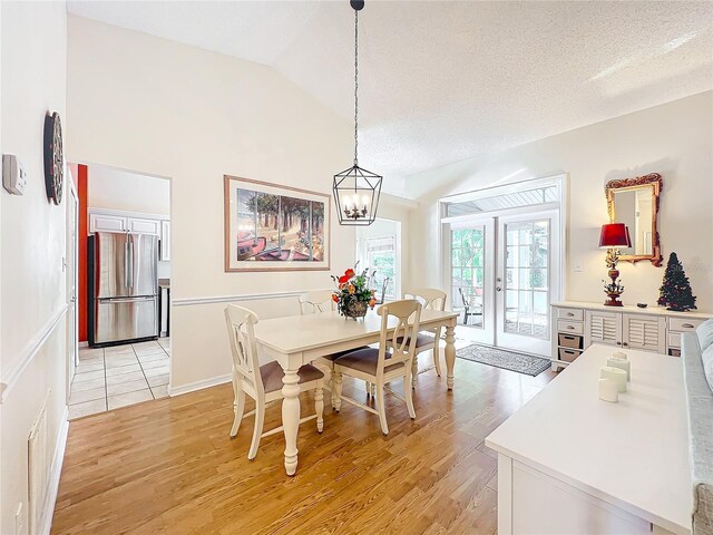 dining area with a textured ceiling, vaulted ceiling, french doors, light wood-type flooring, and a chandelier