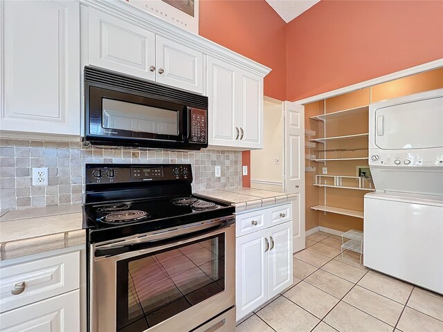 kitchen with electric stove, tile counters, light tile patterned floors, white cabinetry, and stacked washer and dryer