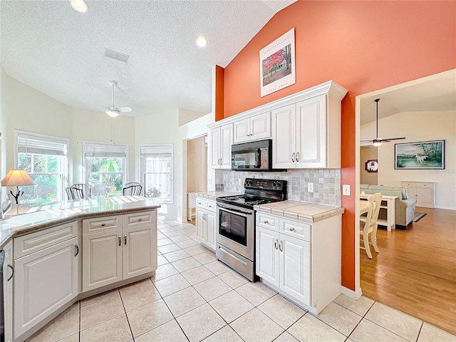 kitchen featuring lofted ceiling, stainless steel electric range, white cabinets, and light tile patterned floors