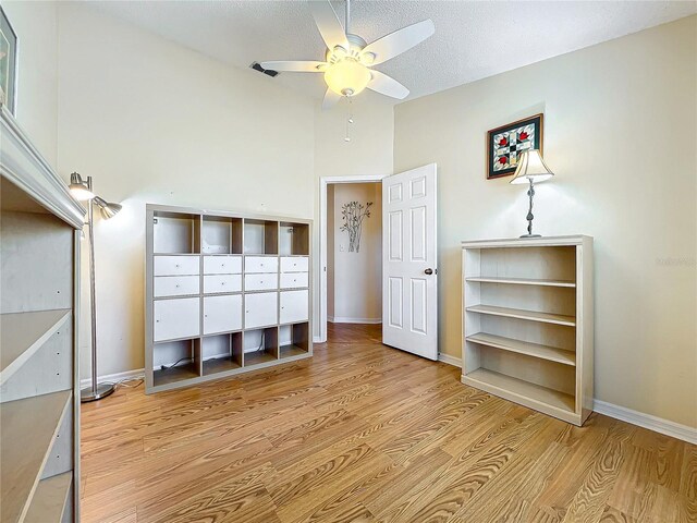 unfurnished bedroom with a towering ceiling, a textured ceiling, ceiling fan, and light hardwood / wood-style flooring