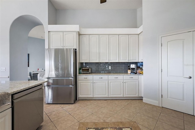 kitchen with a towering ceiling, white cabinets, stainless steel refrigerator, and light tile patterned floors