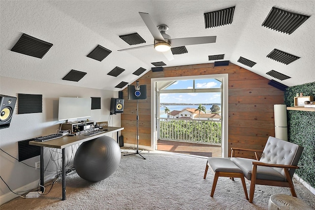 carpeted home office featuring vaulted ceiling, a textured ceiling, wood walls, and ceiling fan