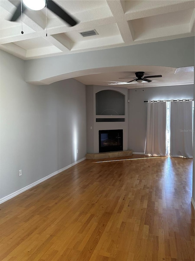 unfurnished living room featuring coffered ceiling, wood-type flooring, ceiling fan, and beam ceiling