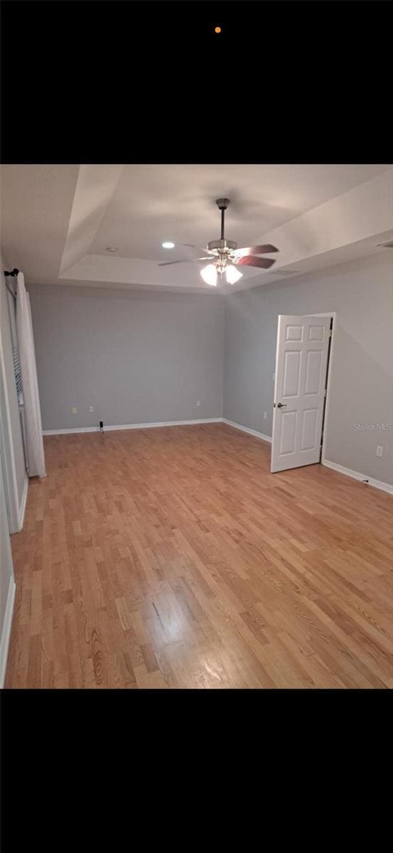 interior space with a raised ceiling, ceiling fan, and light hardwood / wood-style flooring