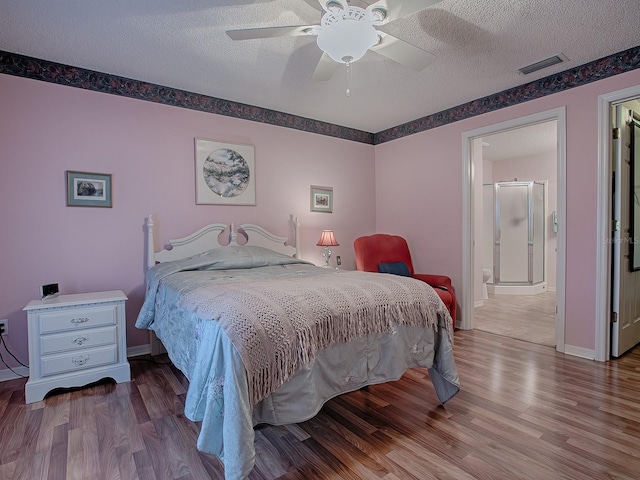 bedroom with ceiling fan, wood-type flooring, ensuite bathroom, and a textured ceiling