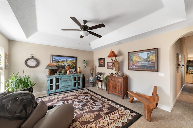 carpeted living room with a raised ceiling and ceiling fan